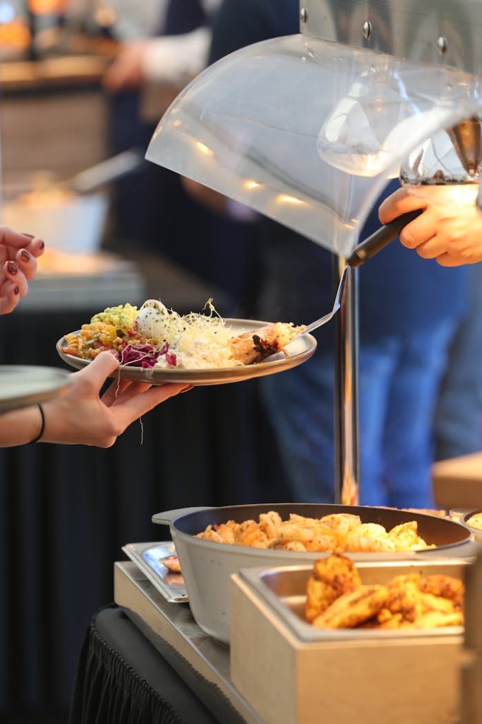A buffet scene showing people serving assorted foods onto plates under warm lighting.
